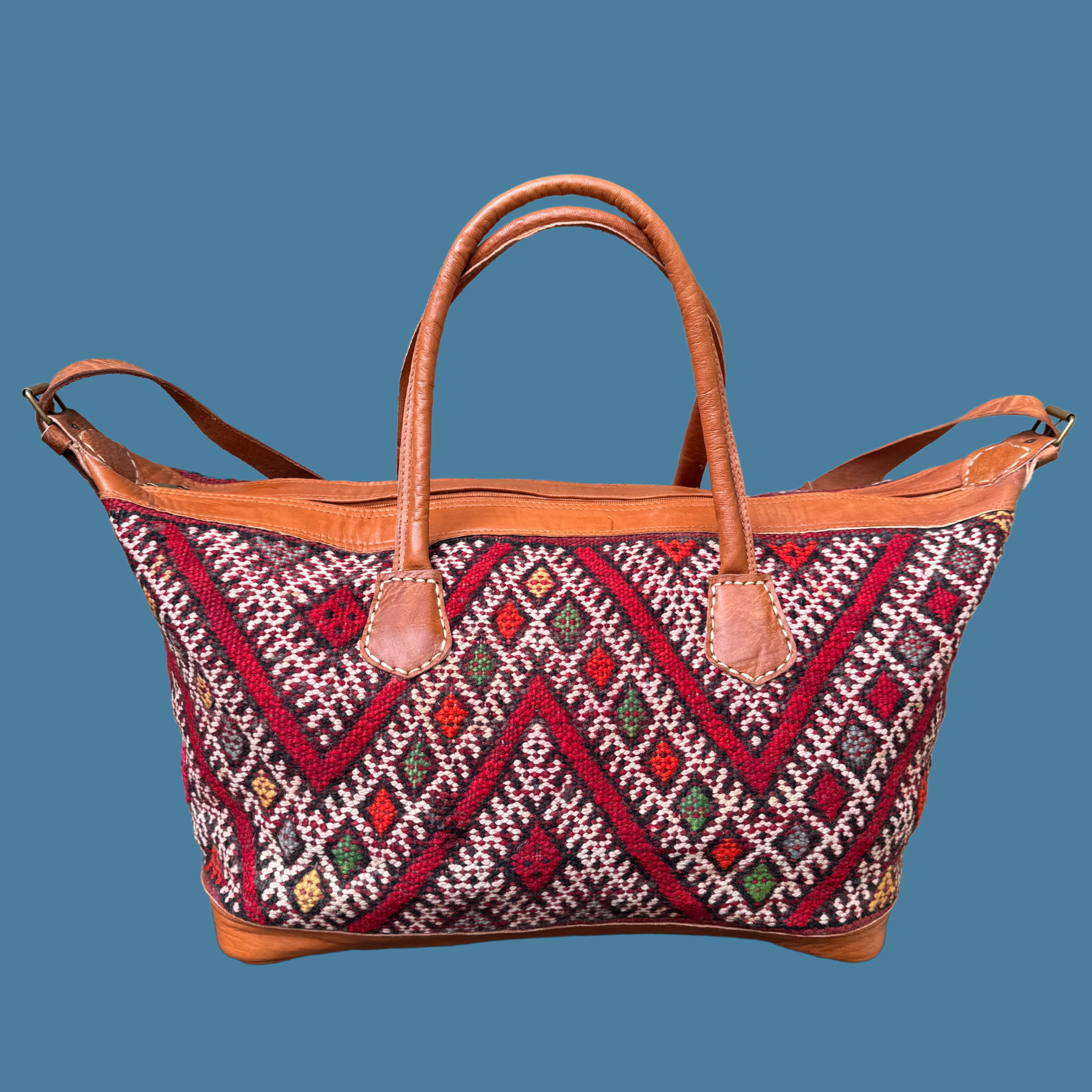 Kilim Weekender with intricate pattern and brown handles on a blue background