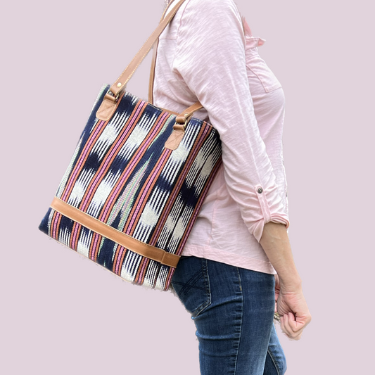 Model wearing Intertwined: Handmade for Good's coral and navy Jaspe Structured Tote over shoulder. 