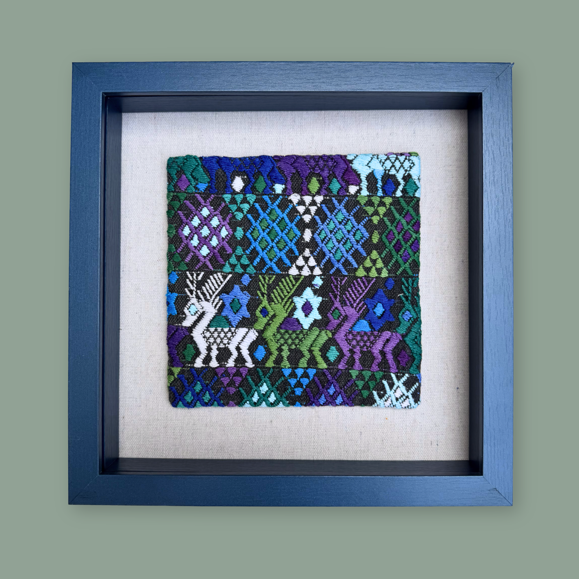 Framed textile art piece with geometric patterns and deer designs on a gray background