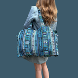 Person carrying a large blue patterned bag on a solid background