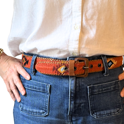 Person wearing a white shirt, orange belt with a pattern, and blue jeans.