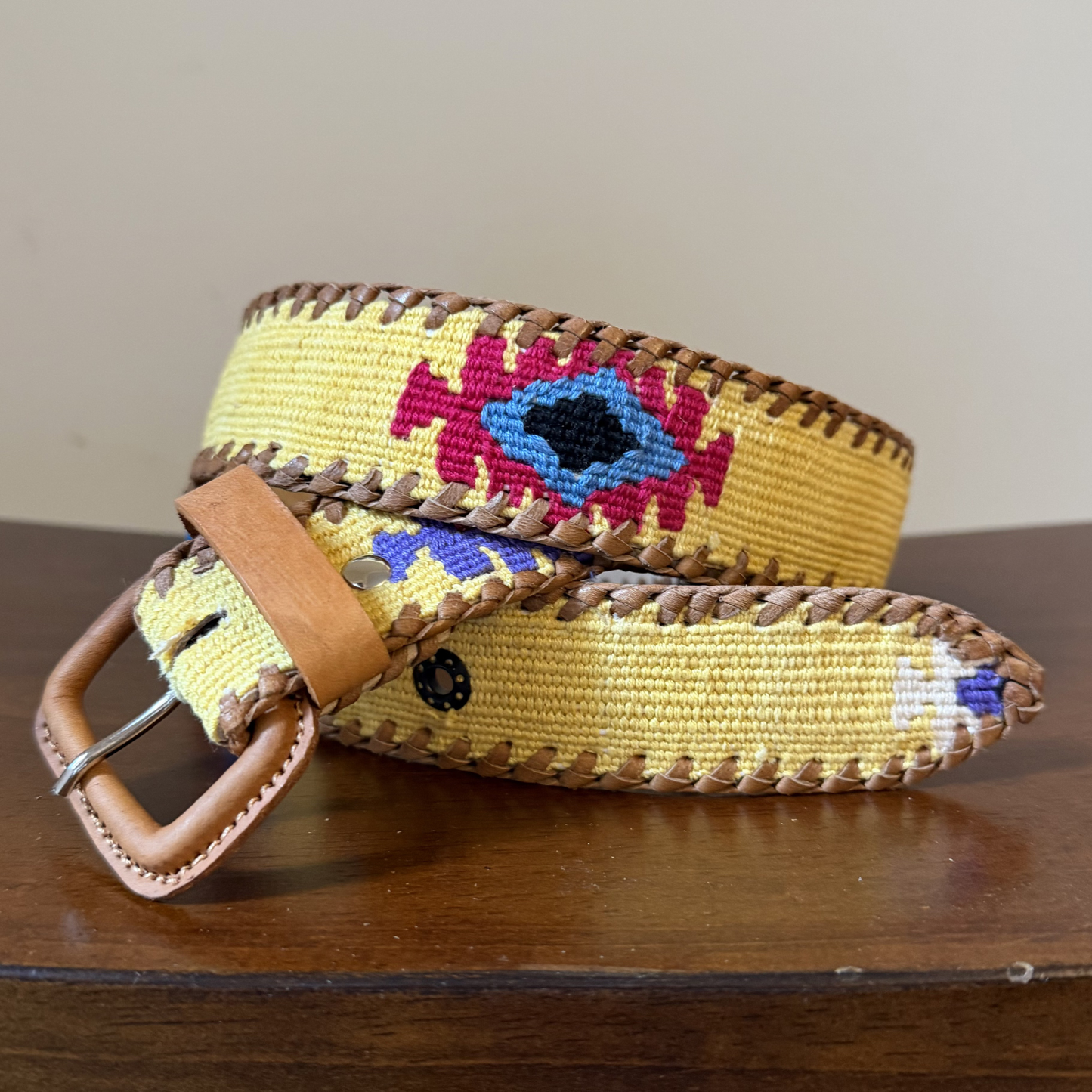Yellow belt with colorful pattern and brown leather buckle on a wooden surface