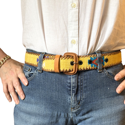 Person wearing a yellow belt with a decorative buckle, white shirt, and blue jeans.