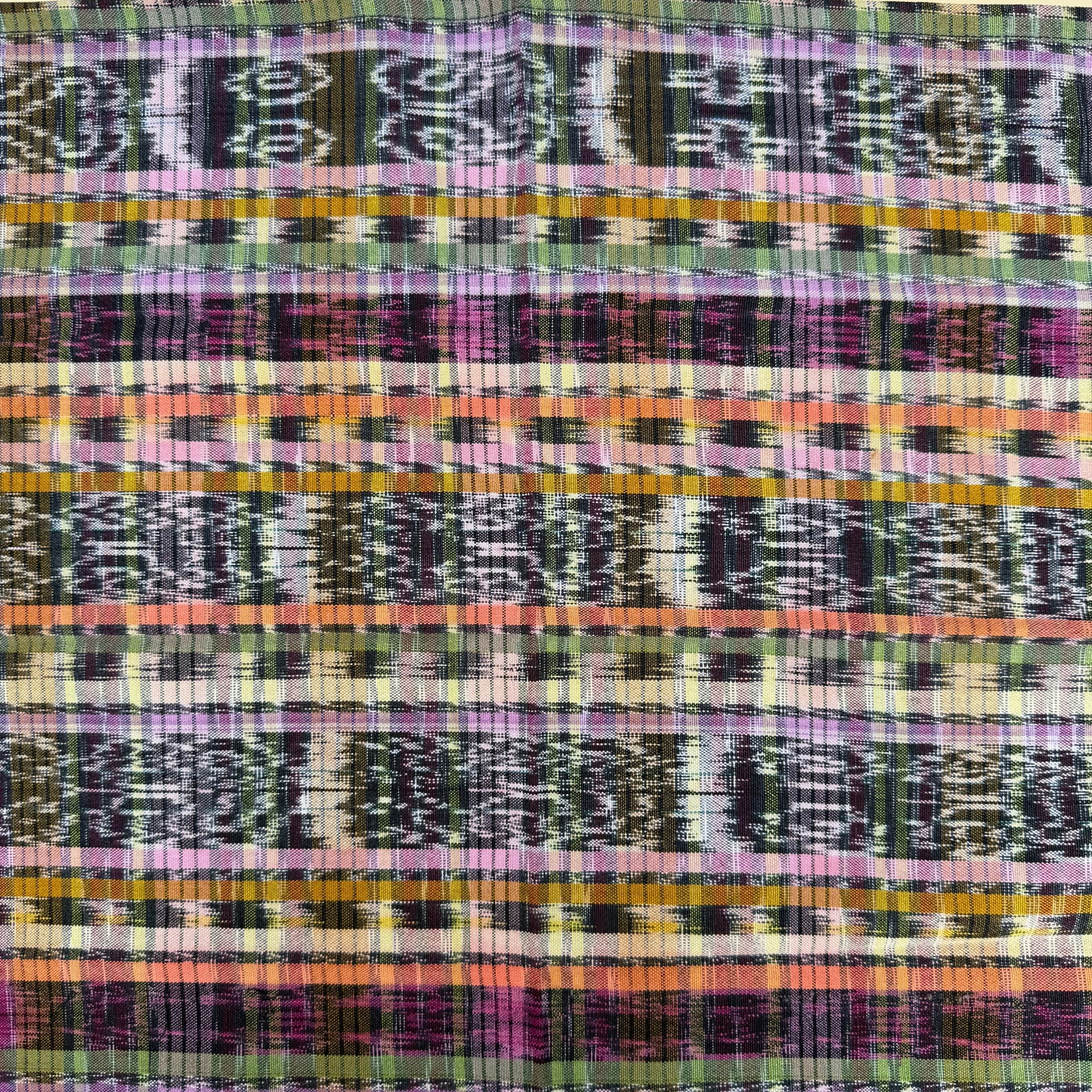 A close-up of a woven textile with horizontal multicolor stripes and geometric patterns in purple, pink, orange, yellow, green, black, and white.