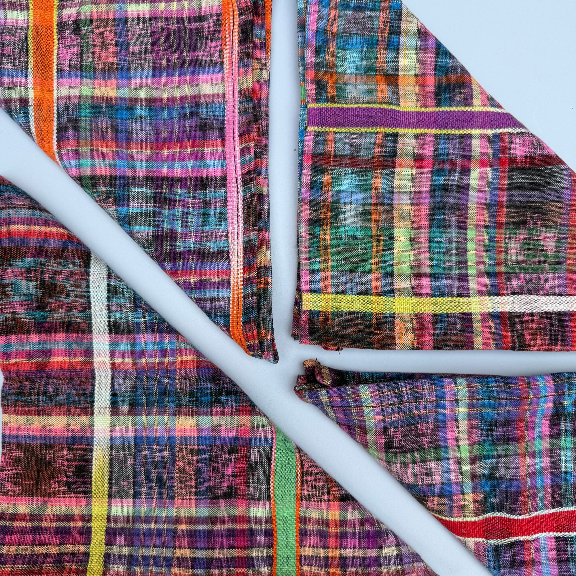 Four colorful ikat plaid woven napkins  laid flat on a light blue-grey background