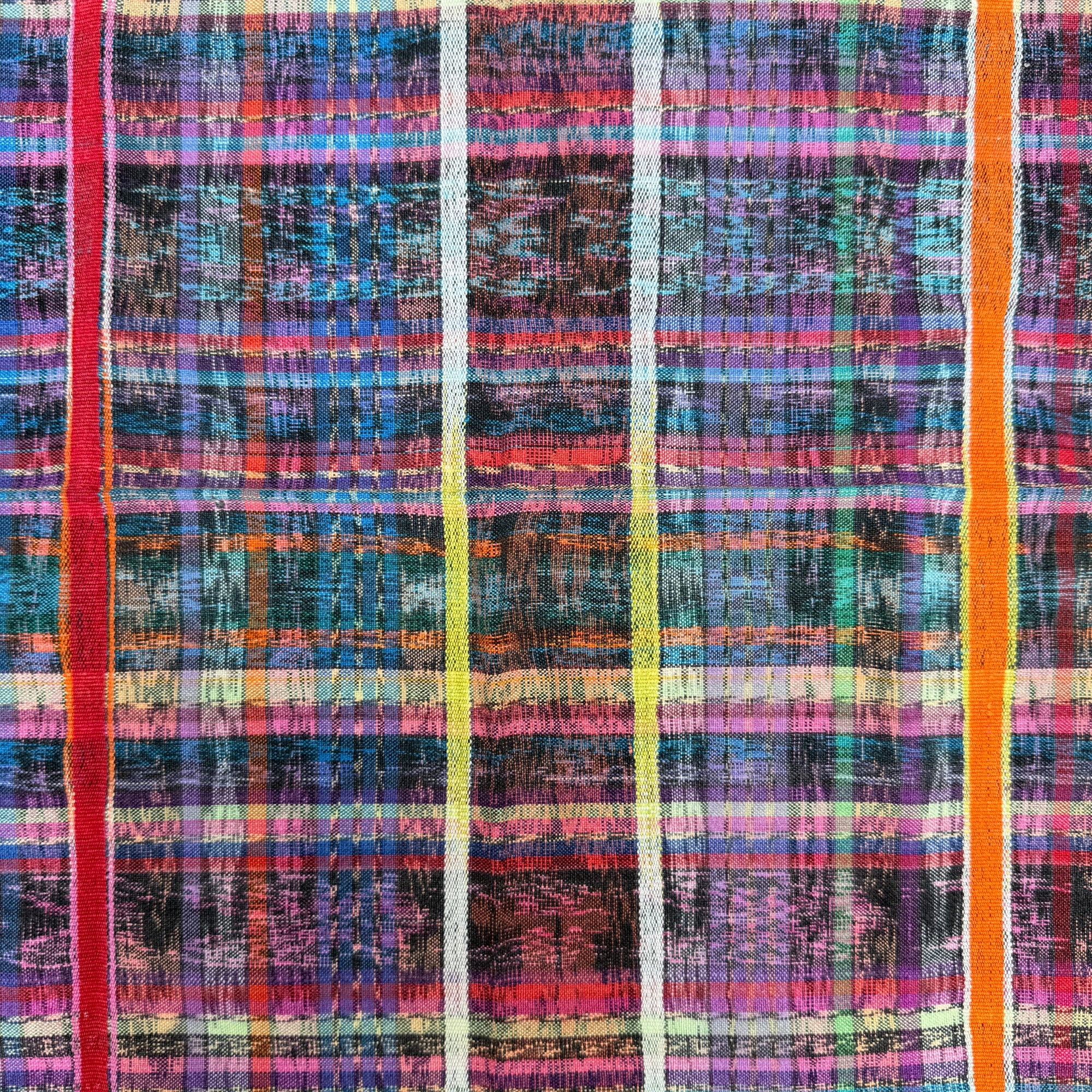 A close-up of a multicolor plaid fabric with vertical stripes in red, orange, yellow, blue, purple, and white over a dark base.