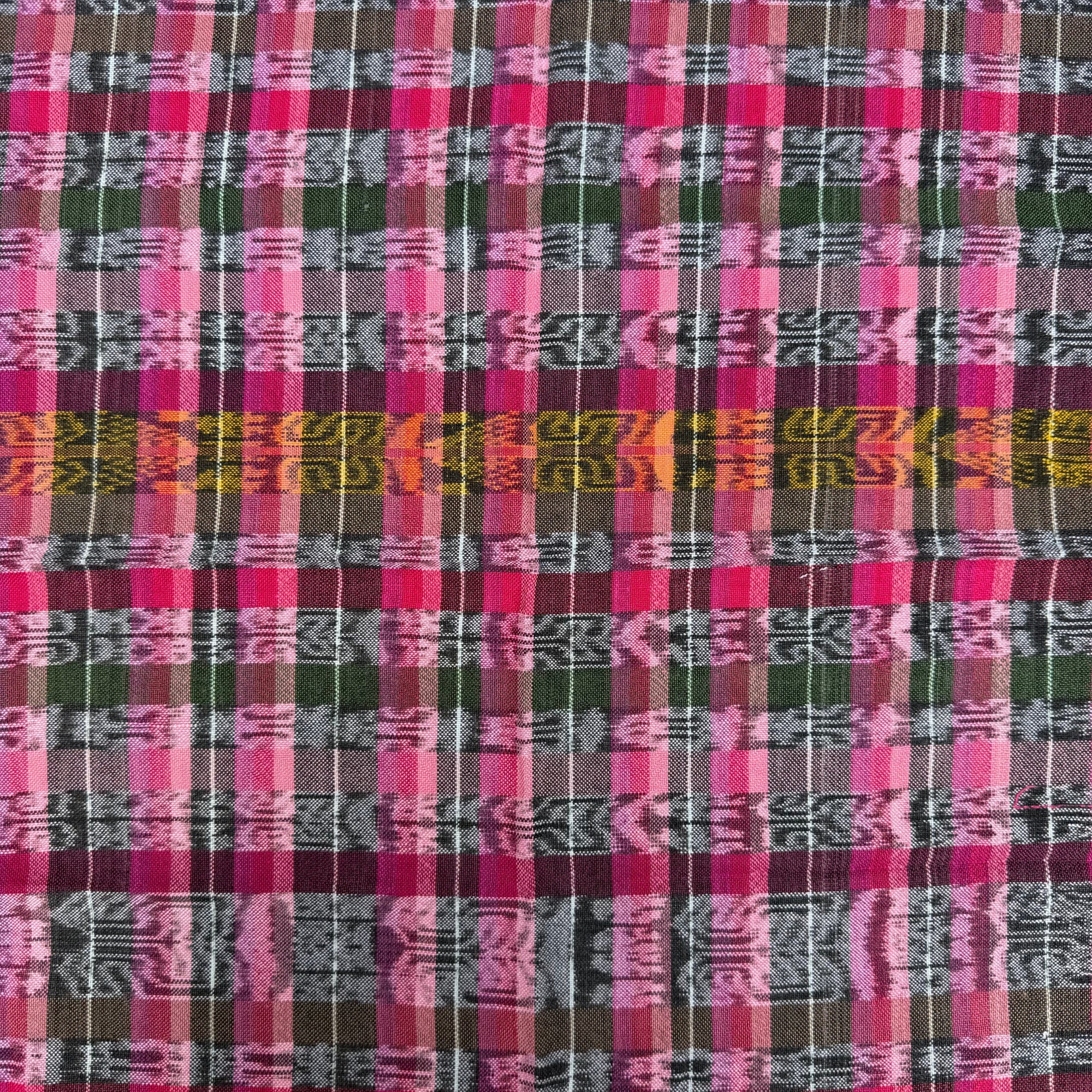 A close-up of a woven textile with a multicolor plaid pattern featuring pink, green, purple, and black stripes with geometric woven motifs.