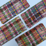 Four folded napkins with a colorful plaid pattern, arranged diagonally on a light blue background.