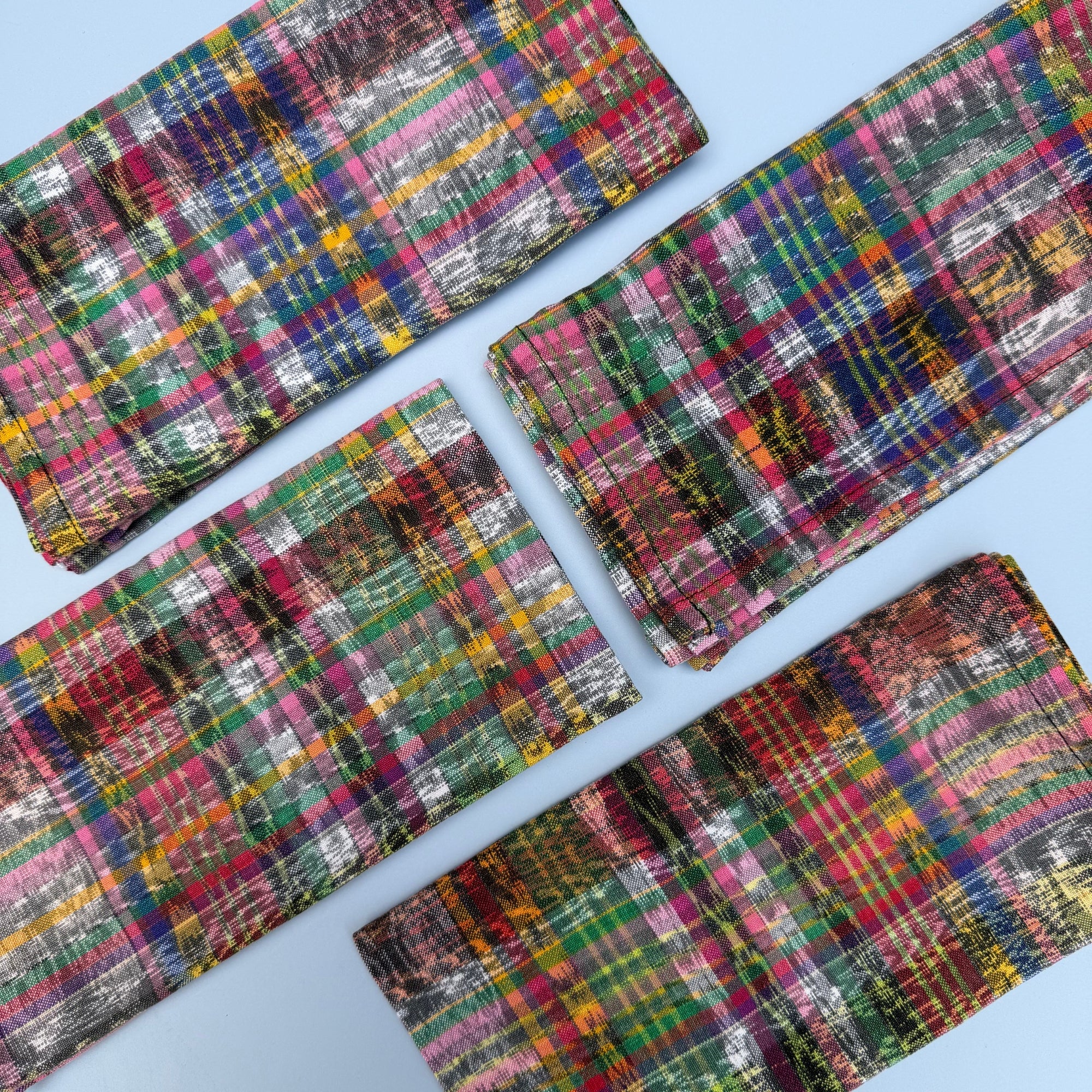 Four folded napkins with a colorful plaid pattern, arranged diagonally on a light blue background.