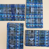 Four folded napkins with blue, navy, green, and white ikat patterns, arranged on a light beige background.
