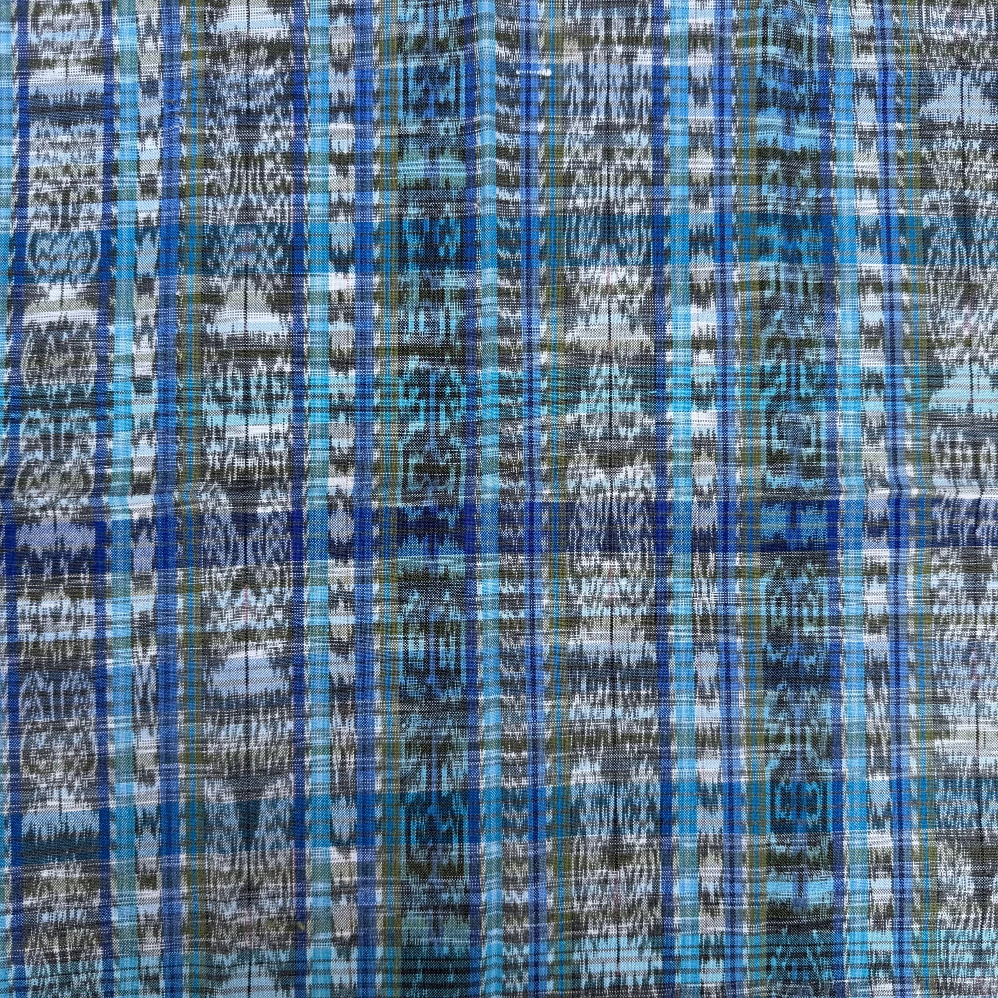 A close-up of a woven fabric with a vertical ikat pattern in shades of blue, gray, black, and white.