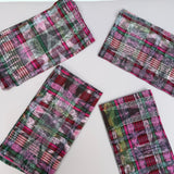 Four rectangular fabric napkins with a colorful plaid ikat pattern in pink, green, red, and white, arranged on a plain white background.