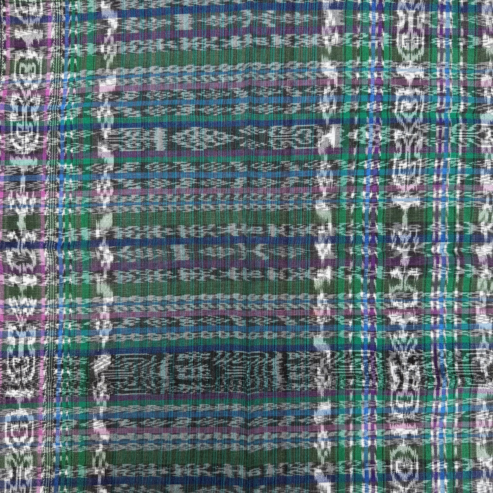 A close-up of a woven textile with a multicolor plaid and geometric pattern in green, blue, purple, white, and black.