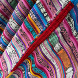 Close-up of a colorful striped textile with woven patterns in pink, blue, teal, orange, yellow, black, and white, crossed by a prominent red embroidered seam.