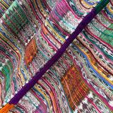 Close-up of a multicolored striped fabric with a thick purple embroidered line running diagonally across the frame.