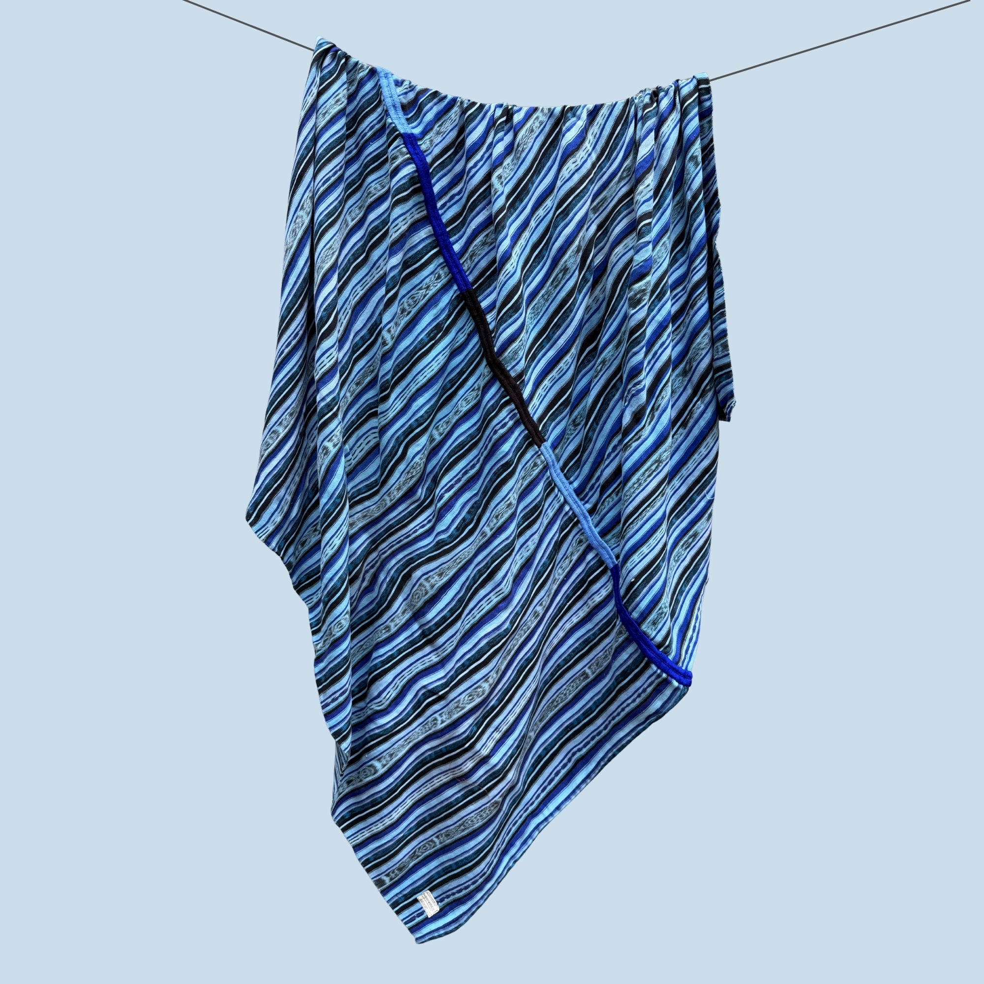 A Carolina blue patterned throw blanket with black and white wavy stripes, hanging from a thin wire against a solid light blue background.