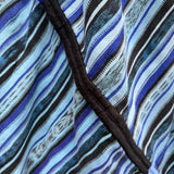 Close-up of a striped textile with blue, black, white, and light blue bands, featuring a black embroidered trim running diagonally across the frame.