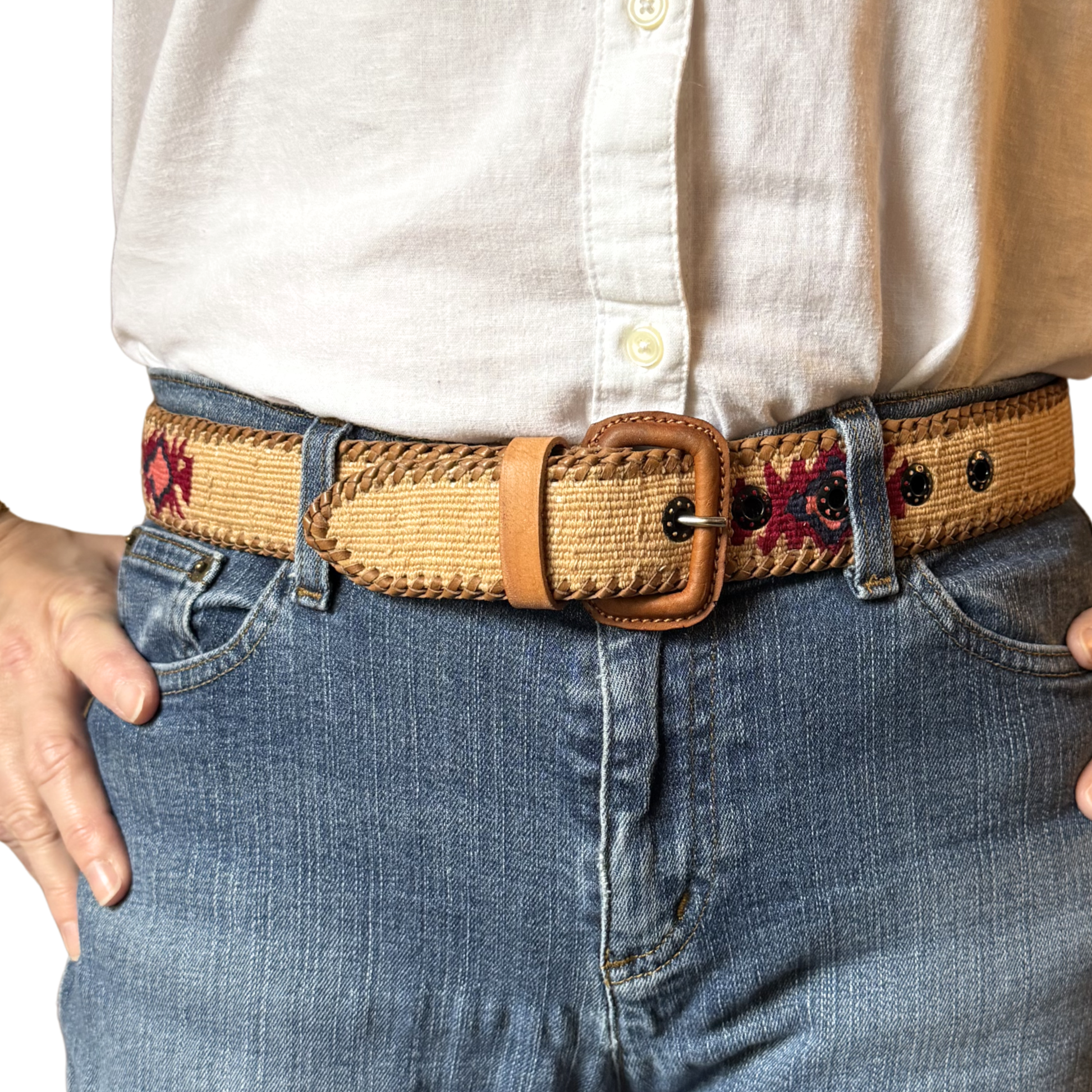 Person wearing a woven belt with floral patterns on jeans and a white shirt.