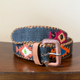 Decorative belt with floral pattern and leather buckle on a wooden surface