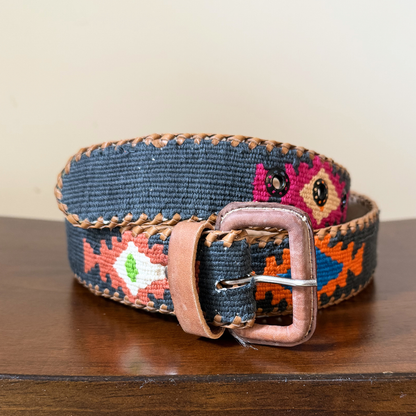 Decorative belt with floral pattern and leather buckle on a wooden surface
