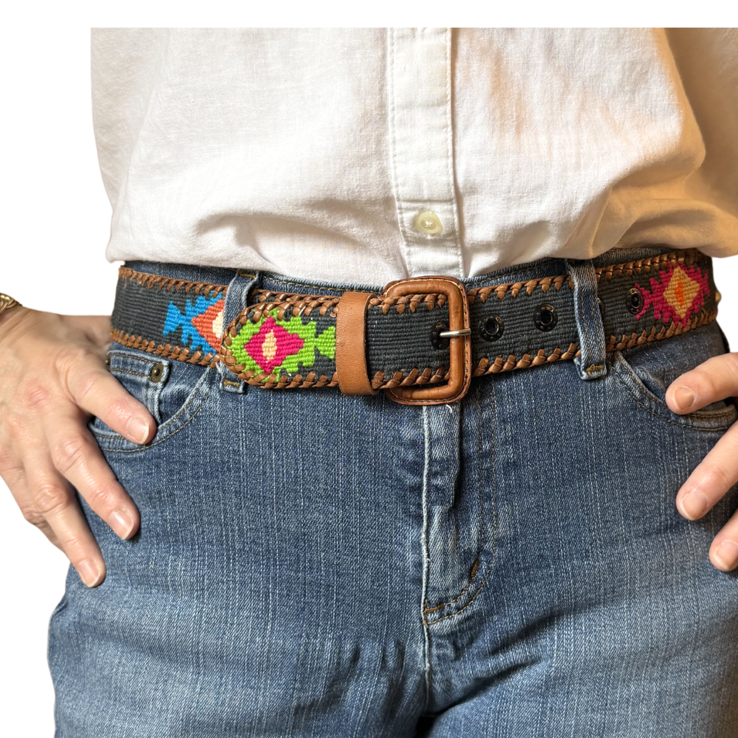 Person wearing a belt with colorful embroidery on jeans against a white background
