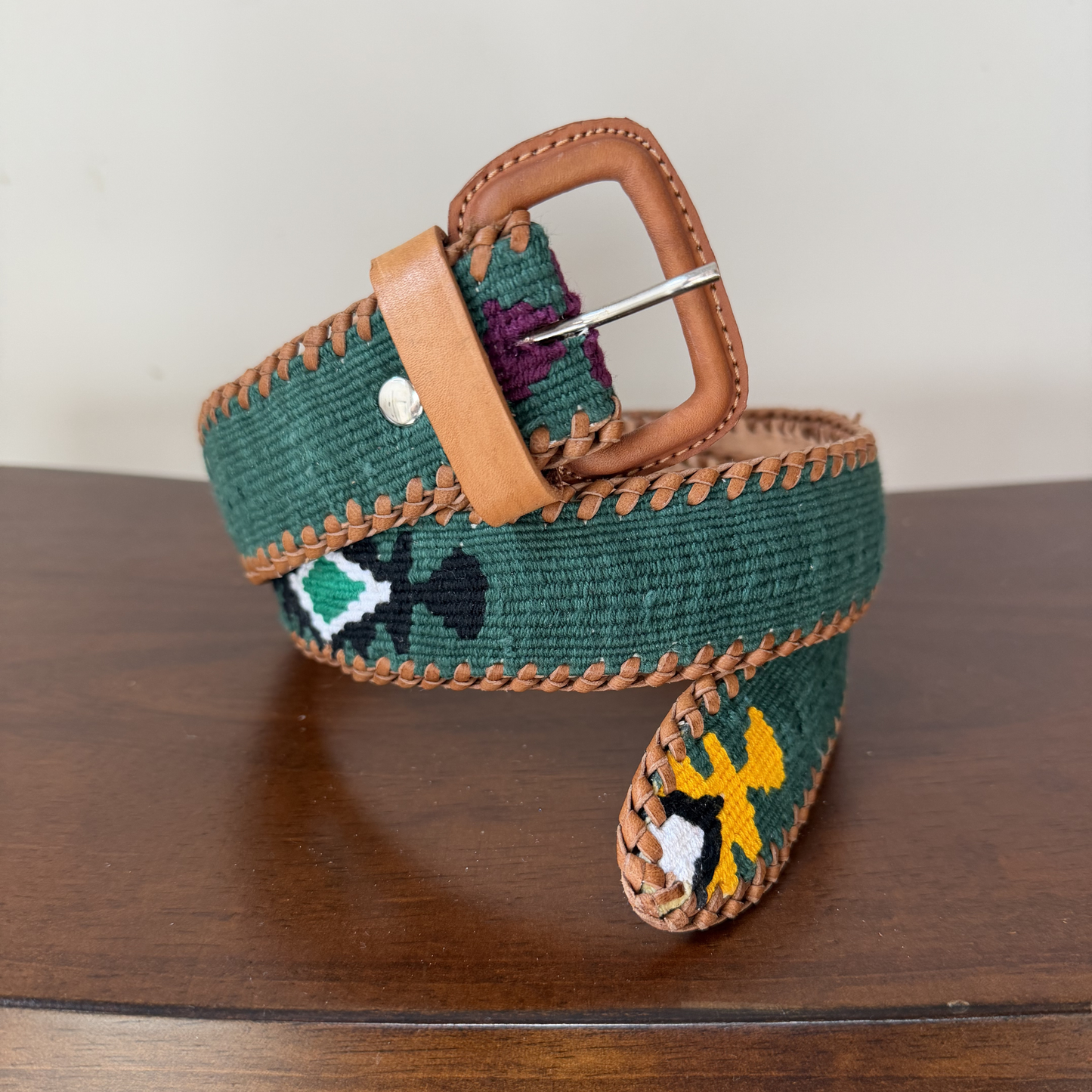 Green belt with brown leather buckle and decorative elements on a wooden surface