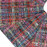 A close-up of a multicolor plaid fabric with a textured, tie-dye-like pattern in shades of pink, blue, red, orange, green, and purple, shown folded on a white background.