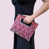 Person holding a pink and black patterned clutch bag against a light pink background