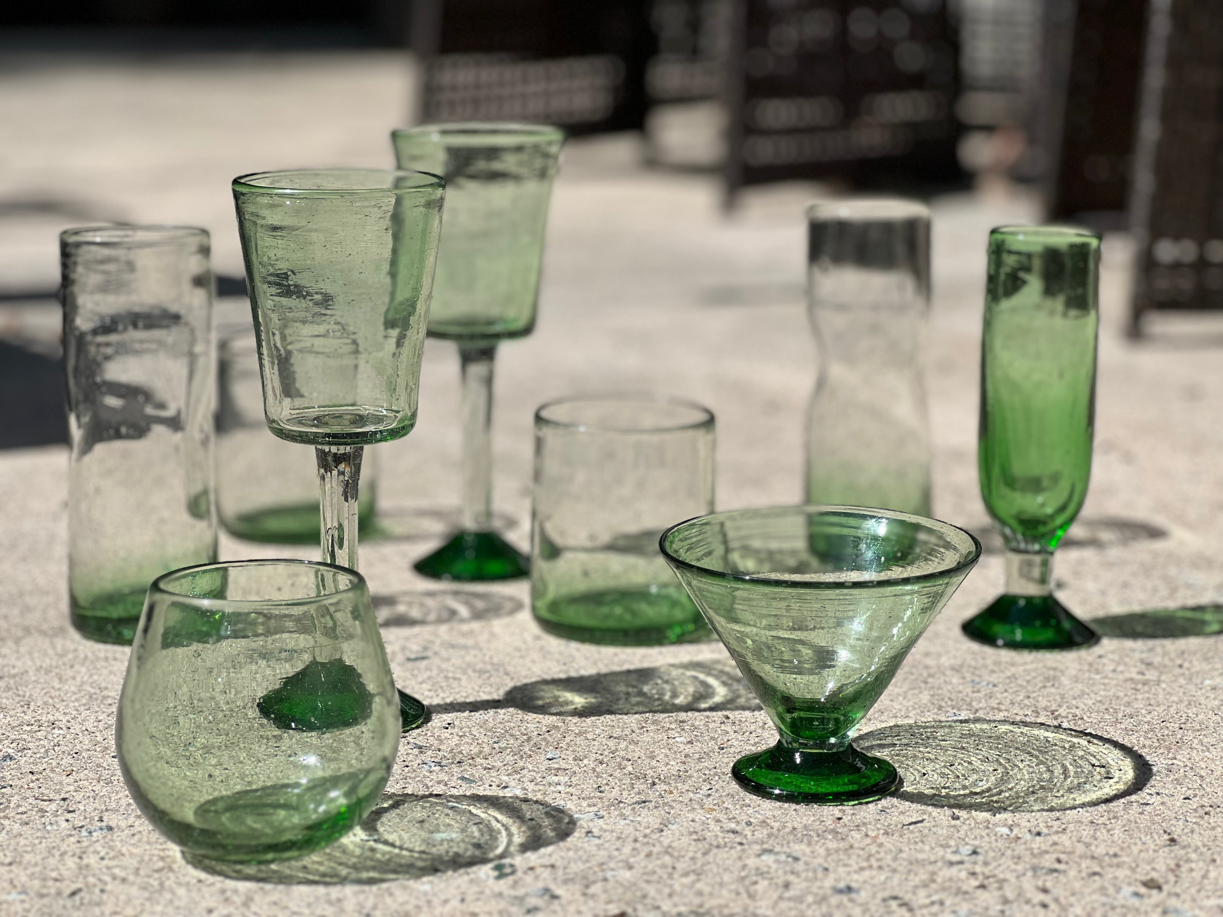 Collection of handblown green stemless wine glasses, champagne glasses, stemless martini glasses on a textured surface