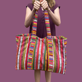Person holding a colorful striped tote bag against a purple background