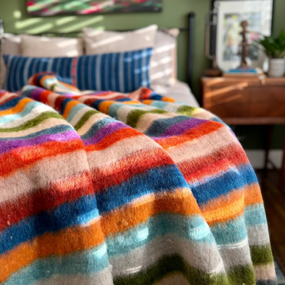 Colorful striped blanket draped over a bed in a bedroom setting.