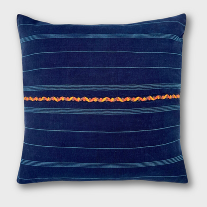 Indigo corte pillow with an orange embroidered line running horizontally across the pillow.