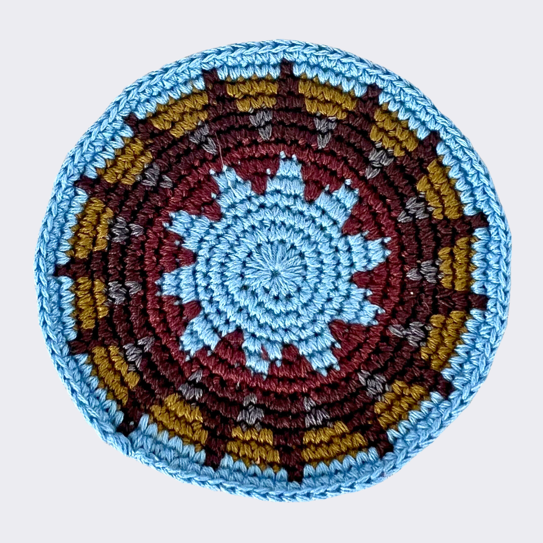 Close up of olive and blue crocheted coaster on light gray background - Intertwined: Handmade for Good
