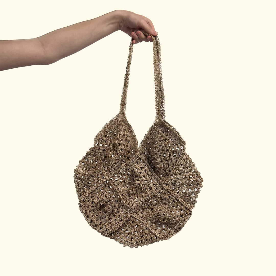 Hemp Crocheted Market Bag being held up against a light yellow background - Intertwined: Handmade for Good