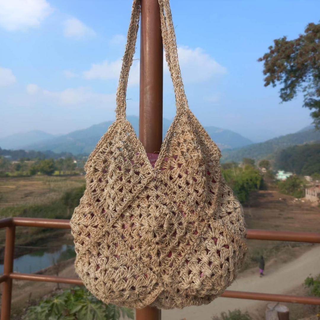 Hemp Crocheted Market Bag hanging on a pole with a landscape scene in the background - Intertwined: Handmade for Good