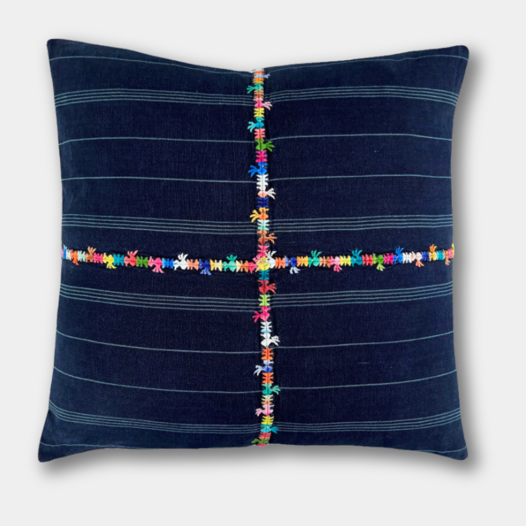 Indigo corte pillow on a light gray background, with a multicolor embroidered cross across the front.