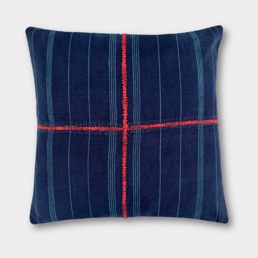 Indigo corte pillow on a light gray background, with a red embroidered cross spanning the front of the pillow. 