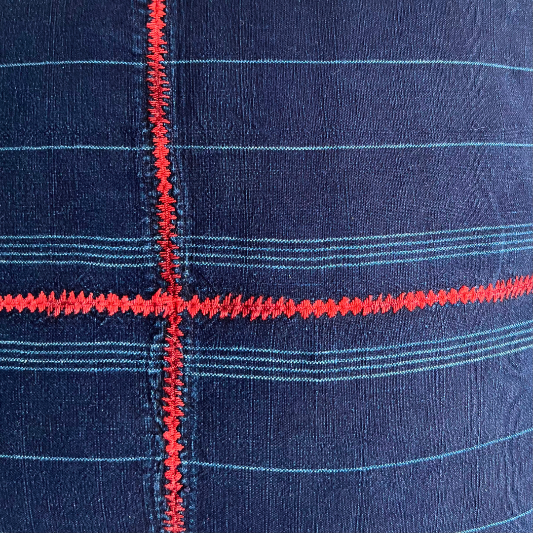 Close up of indigo corte pillow, with red cross embroidery in the center.