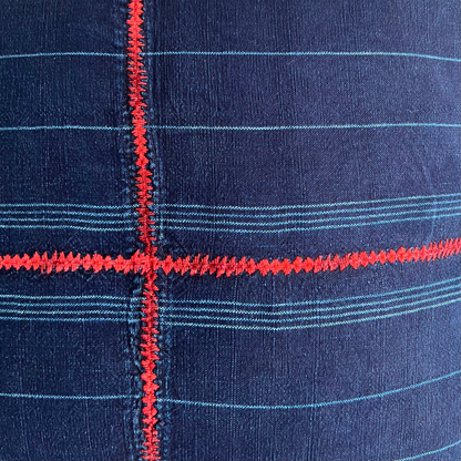 Close up of indigo corte pillow, with red cross embroidery in the center.