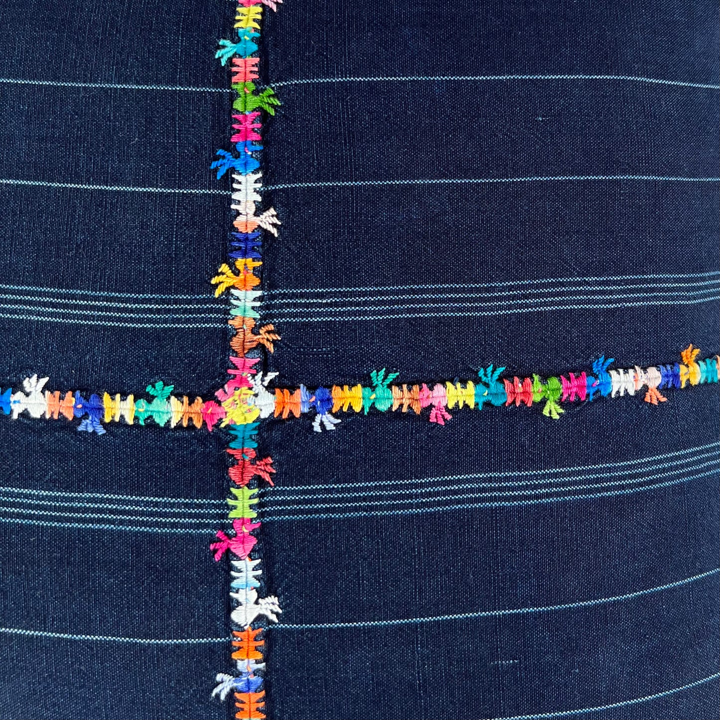 Close up of the multicolor embroidered cross on the indigo corte pillow.