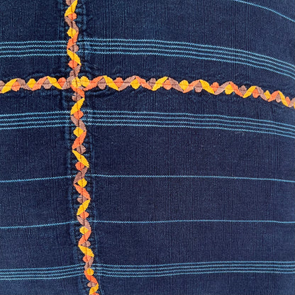 Close up of the orange embroidered cross on an indigo corte pillow.